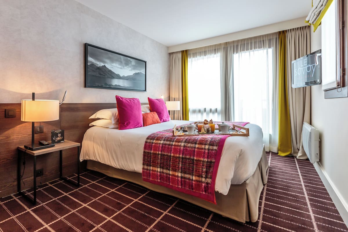Een hotelkamer met een bed, een nachtkastje met een lamp, een dienblad met ontbijtartikelen en een schilderij aan de muur.