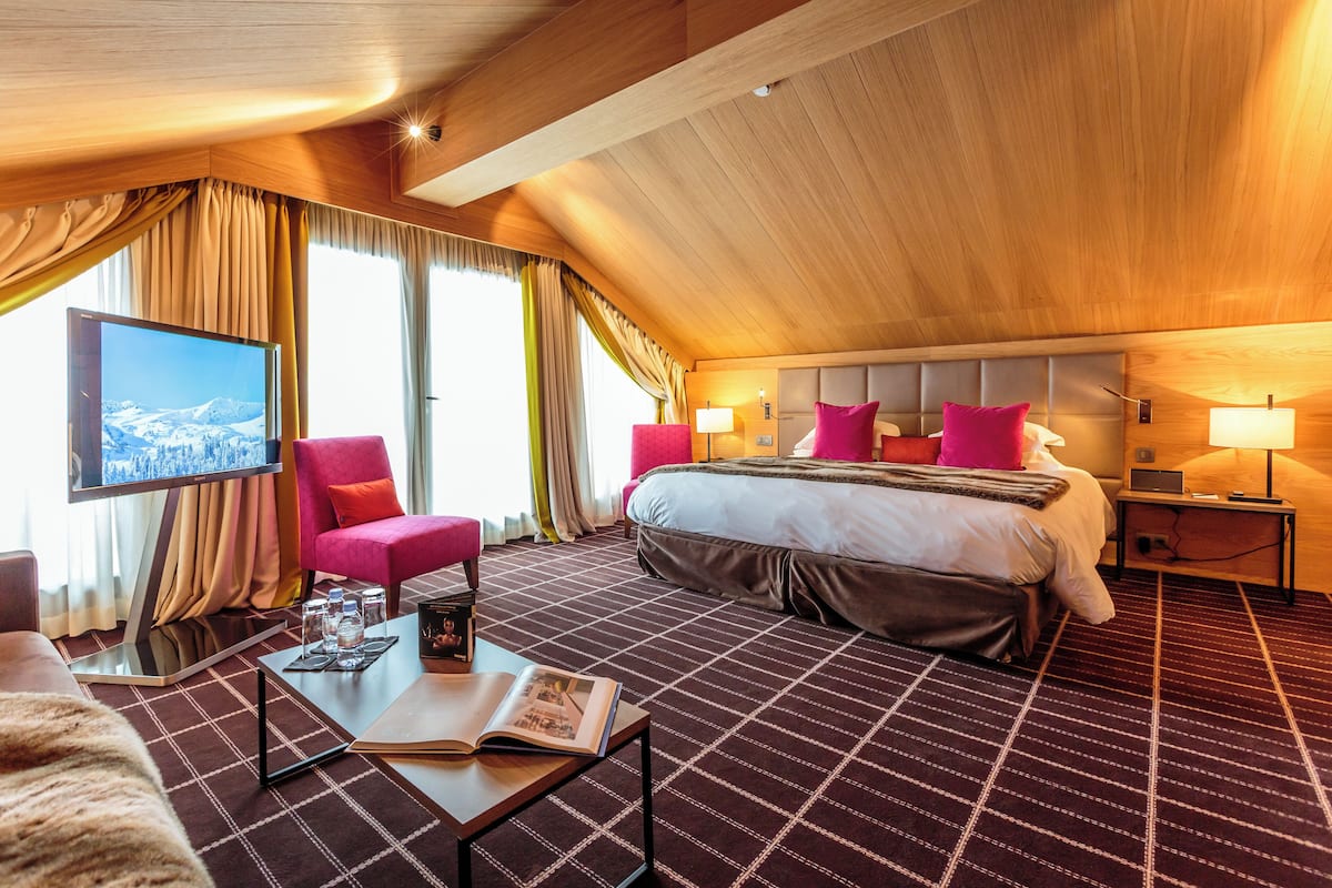 Een hotelkamer met een groot bed, een televisie, een bureau met een tijdschrift, en uitzicht op een besneeuwd landschap.