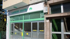 Une auberge de jeunesse à la façade verte et blanche, ornée du logo Shell, et affichant un panneau indiquant les disponibilités des chambres.