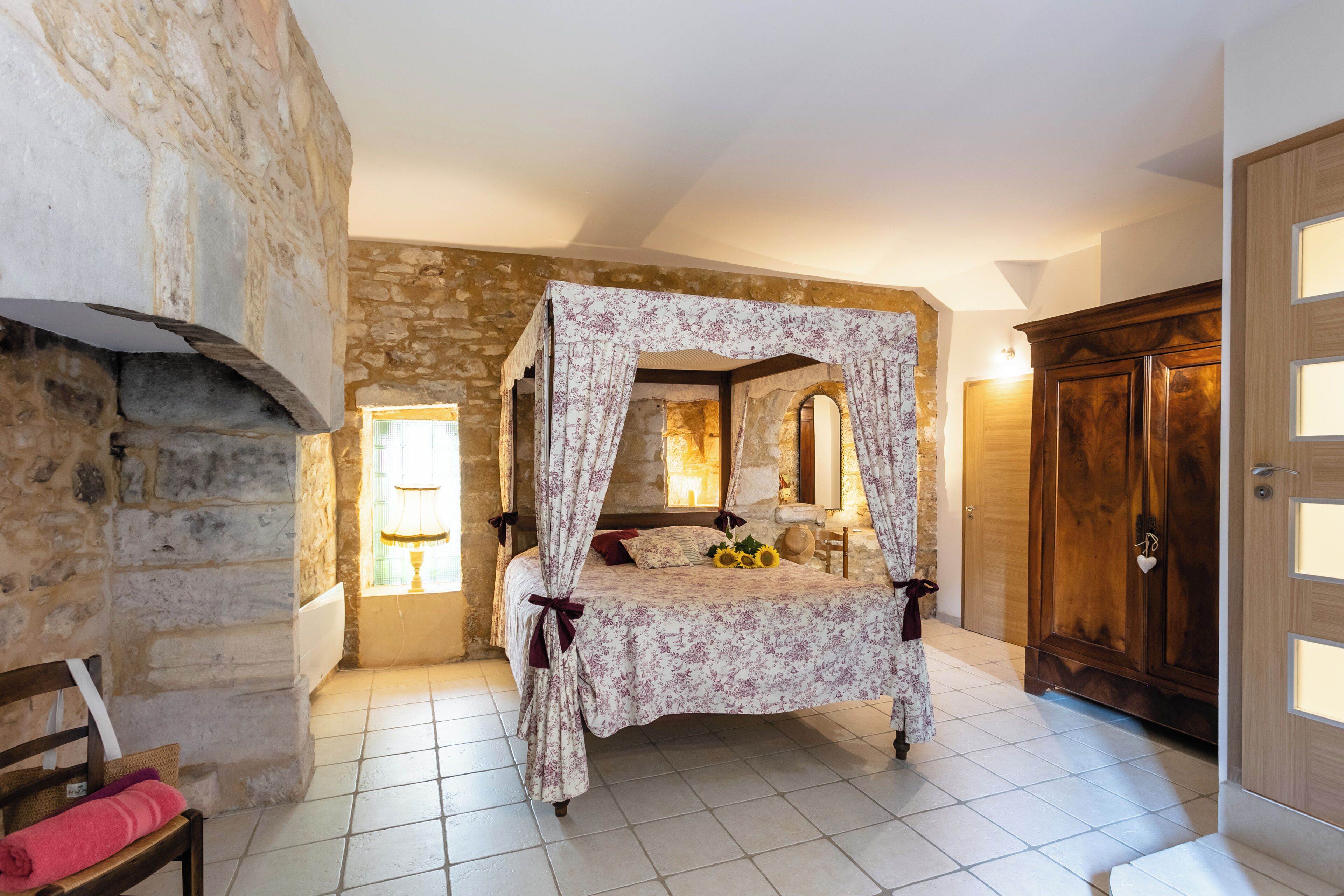 Ein Schlafzimmer mit Steinwand, einem Himmelbett, einem Holzschrank und einem Fliesenboden.