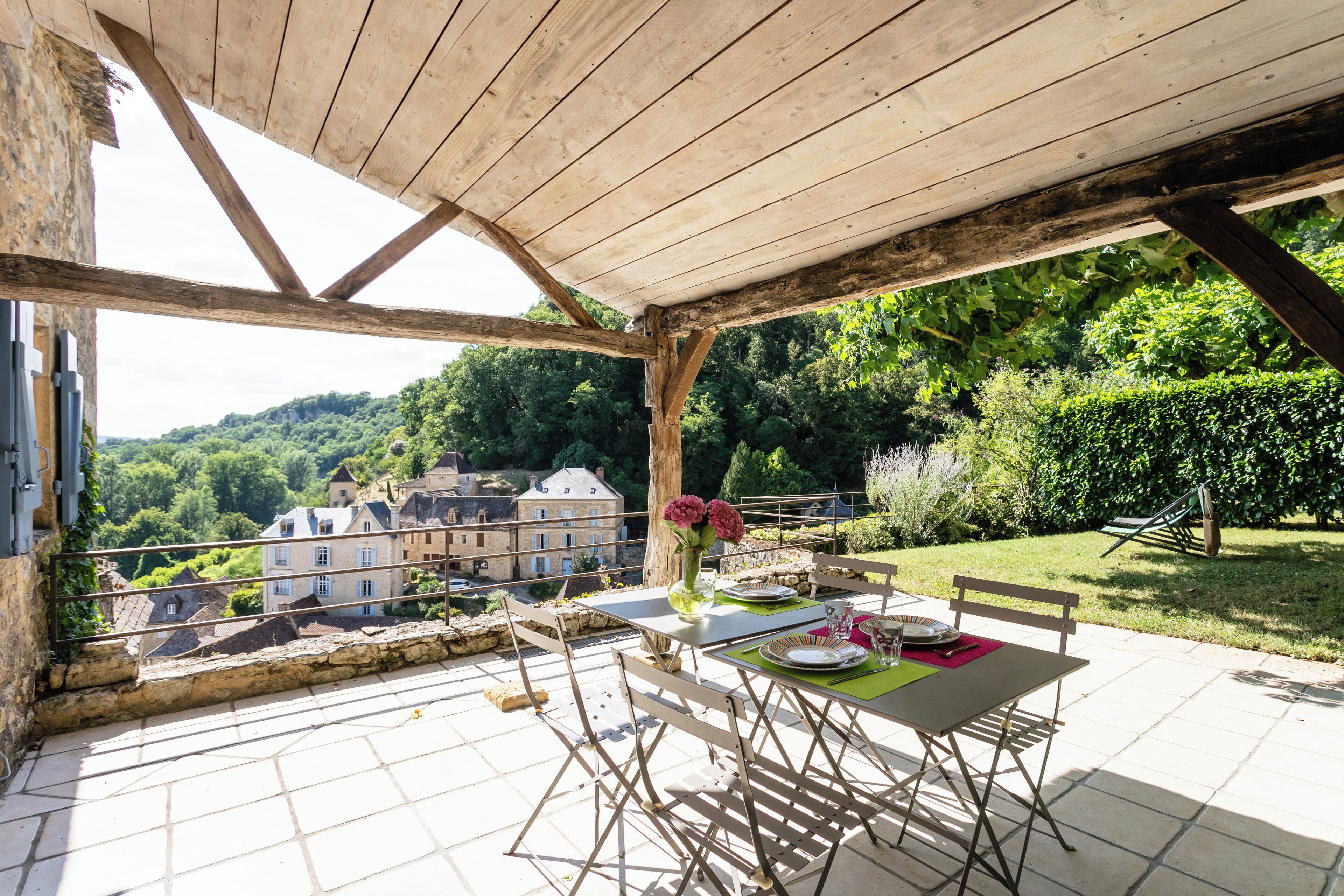 An outdoor patio with a table set for dining, overlooking a scenic view of buildings and greenery.