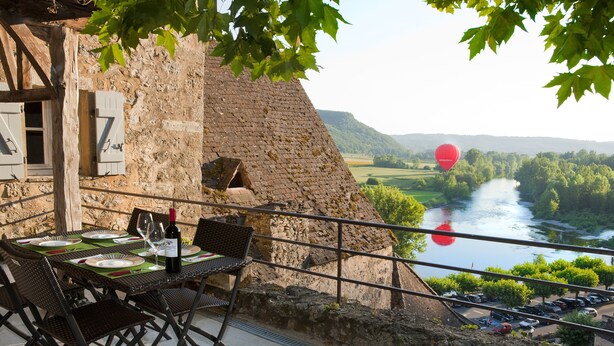 Un comedor con una mesa lista para dos personas, con vista a un río y follaje.