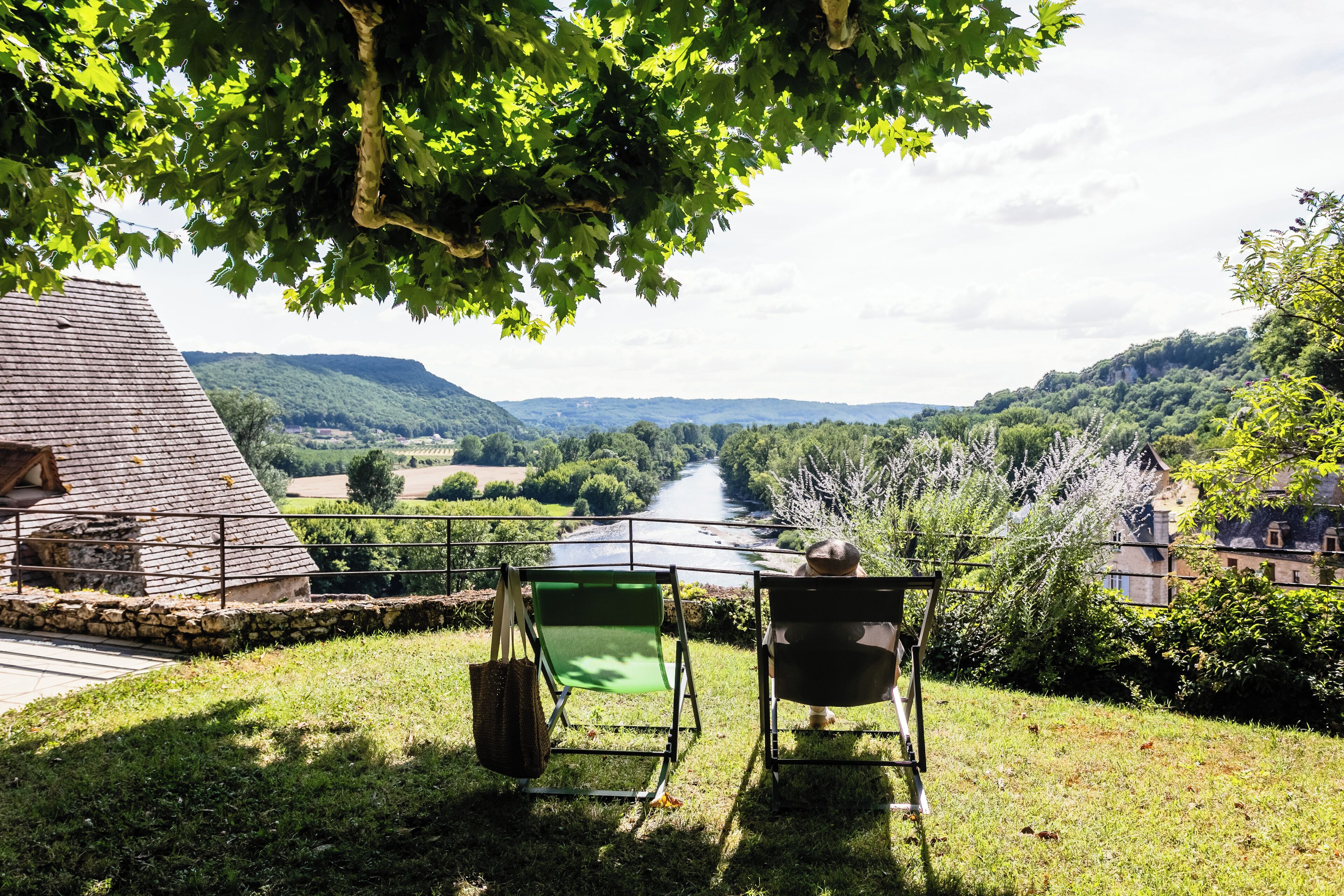 A view from a balcony overlooking a river, with two chairs and a table under a tree.