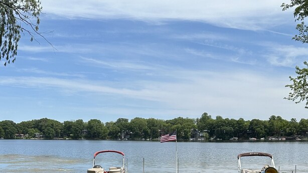 A lakeside deck with two boats docked, a flag, and a grassy area. - Lakehouse with Pontoon, Deck, Firepit, Paddle Boards, Grill & more INCLUDED!!  (Valparaiso)