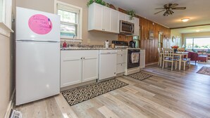 A kitchen with white cabinets, a refrigerator, a microwave, and a dishwasher. There is a ceiling fan and a dining area with a table and chairs. - Lakehouse with Pontoon, Deck, Firepit, Paddle Boards, Grill & more INCLUDED!!  (Valparaiso)