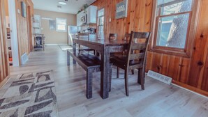 A dining area with a wooden table and chairs, a kitchen in the background, and a sign that reads "LAKE HOUSE". - Lakehouse with Pontoon, Deck, Firepit, Paddle Boards, Grill & more INCLUDED!!  (Valparaiso)