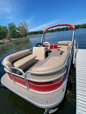 A red and beige pontoon boat docked at a pier with a canopy, equipped with a steering wheel, seating, and a wakeboard. - Lakehouse with Pontoon, Deck, Firepit, Paddle Boards, Grill & more INCLUDED!!  (Valparaiso)