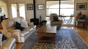 A living room with a beige leather sofa, a wooden coffee table, a patterned rug, a fireplace, and a large window with a view of the outdoors.