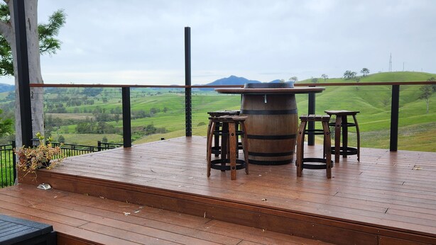 A wooden deck with a table and chairs, overlooking a green landscape with hills.