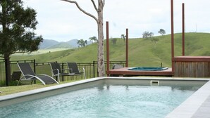 A rectangular swimming pool with a hot tub, surrounded by lounge chairs and a wooden deck.