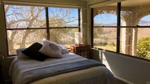 A bedroom with a large bed, two windows, and a view of trees and hills.