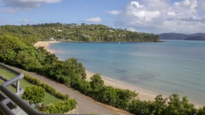 A coastal view with a beach, lush greenery, and houses on a hillside.