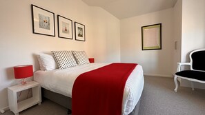 Une chambre à coucher avec un lit, une table de chevet, une chaise et des tableaux encadrés accrochés au mur.