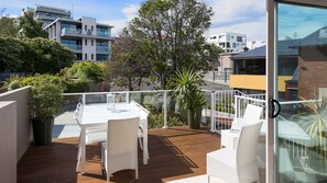A modern outdoor deck with a white table and chairs, surrounded by lush greenery and overlooking a cityscape. - Red Door Penthouse in Battery Point (Battery Point)