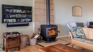 A cozy living room with a fireplace, a flat-screen TV displaying TV shows, and a wicker sofa. - Woodlands at Beachview by HolidayCo. (MACMASTERS BEACH)