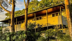 A two-story building with a yellow facade, surrounded by dense greenery and trees. - Woodlands at Beachview by HolidayCo. (MACMASTERS BEACH)
