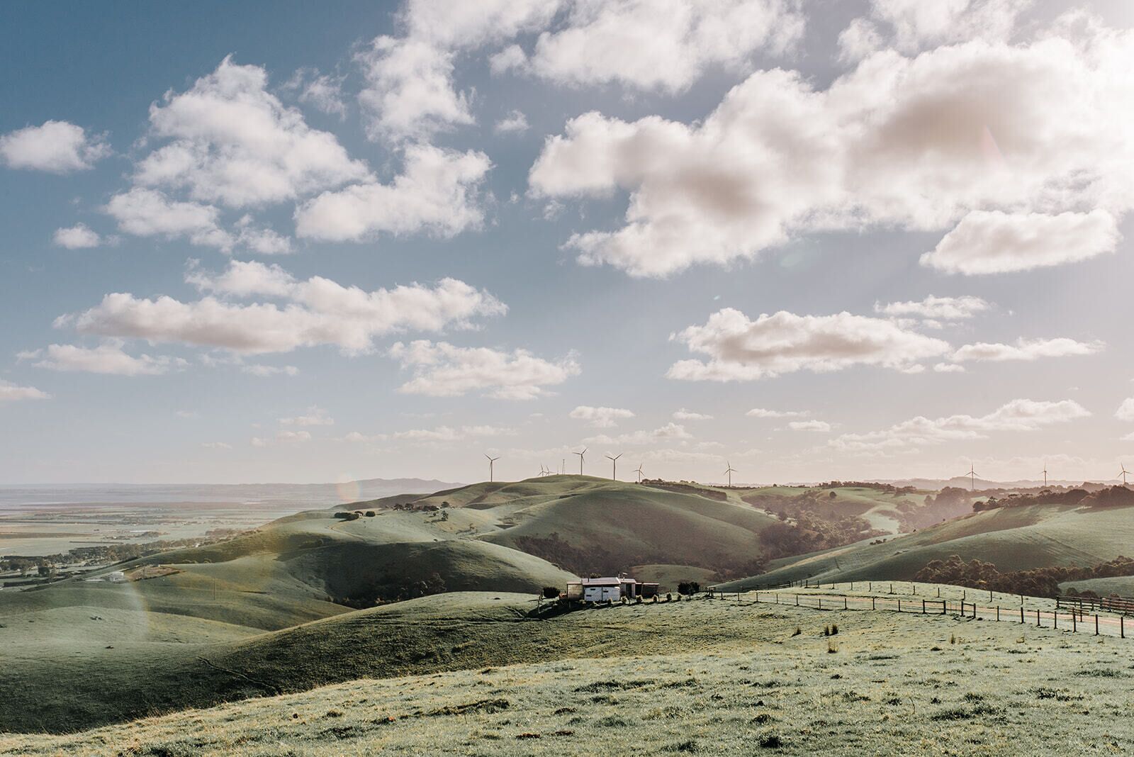 A landscape with rolling hills, wind turbines, and a fenced area with a building.