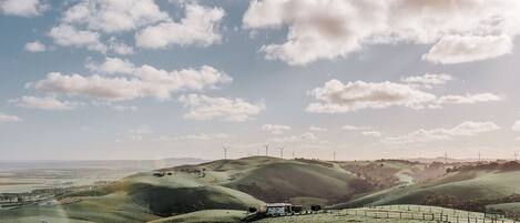 A landscape with rolling hills, wind turbines, and a fenced area with a building.