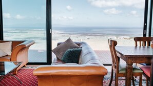 A room with a large sliding glass door leading to a beach view, a leather sofa, a wooden dining table, and a glass coffee table. - 360o views incl. The Prom, Bass Strait and Strzelecki Ranges (Hazel Park)
