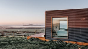 A modern cabin with a large window, a wooden deck, and a view of the landscape. - 360o views incl. The Prom, Bass Strait and Strzelecki Ranges (Hazel Park)