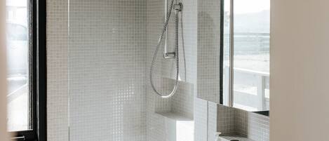 A modern bathroom with a walk-in shower, a large mirror, and a white sink.