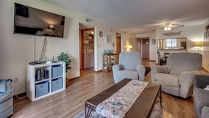 Una sala de estar con televisor de pantalla plana, un sofá, una mesa de centro y una estantería.