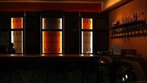 A bar area with a counter, shelves with bottles, and a wall with a sign. - Hotel Alcazar De Doña Victoria (Cobán)