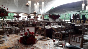 A tented outdoor dining area with tables set for a formal event, featuring floral centerpieces and elegant table settings. - Hotel Alcazar De Doña Victoria (Cobán)