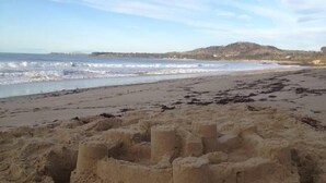 Une plage de sable avec un grand château de sable au premier plan et des vagues qui déferlent à l’arrière-plan.