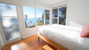 Une chambre avec une grande fenêtre donnant sur la mer et les arbres.