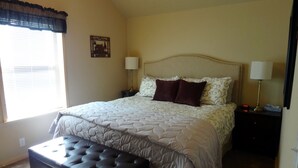 A neatly arranged bedroom with a large bed, two bedside lamps, a small bedside table, and a bench at the foot of the bed.