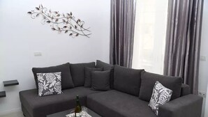 A modern living room with a grey sectional sofa, a black coffee table with a tray of glasses and a bottle, and a decorative metal wall piece.