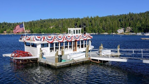En stilleliggende båd ved et fortøjningsanlæg med et amerikansk flag, omgivet af roligt vand og en skovklædt kystlinje.