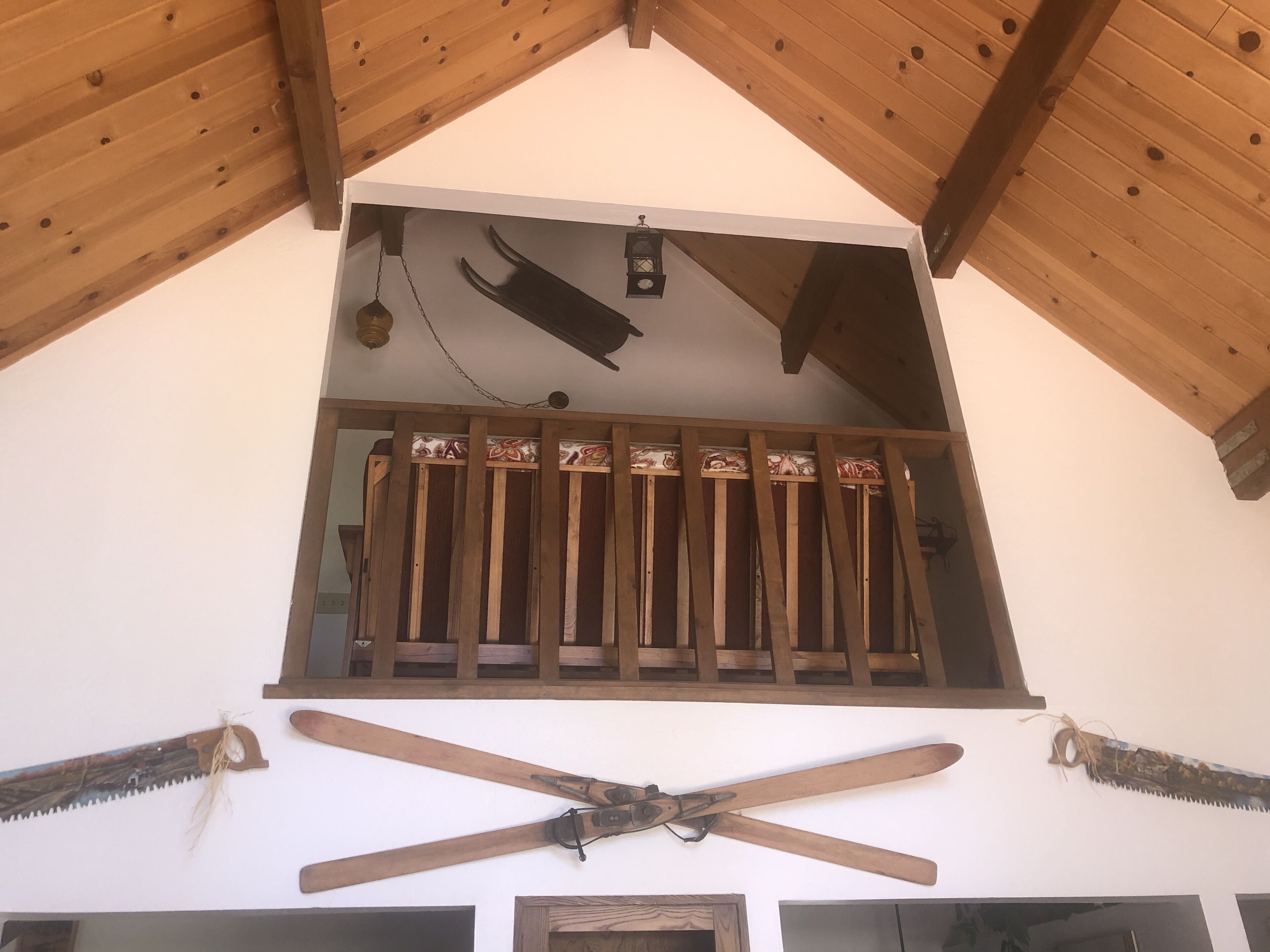 Un balcon en bois agrémenté d’une balustrade décorative, d’une lanterne suspendue et de deux paires de skis en bois fixés au mur en dessous.