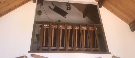 Un balcon en bois agrémenté d’une balustrade décorative, d’une lanterne suspendue et de deux paires de skis en bois fixés au mur en dessous.