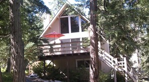 A two-story cabin with a balcony, surrounded by trees.