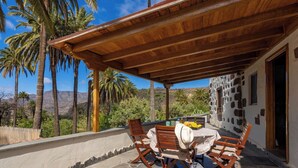 A covered outdoor seating area with a table and chairs, overlooking a mountainous landscape with palm trees. - GC0242 Holiday cottage with private pool in Santa Lucía (Santa Lucía de Tirajana)