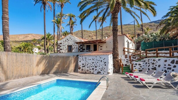 A swimming pool with lounge chairs, palm trees, and a mountain in the background. - GC0242 Holiday cottage with private pool in Santa Lucía (Santa Lucía de Tirajana)