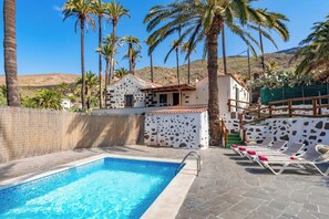 A swimming pool with lounge chairs, palm trees, and a mountain in the background.