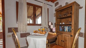 A dining area with a table set for breakfast, a wooden cabinet with books, and a window with curtains. - GC0242 Holiday cottage with private pool in Santa Lucía (Santa Lucía de Tirajana)