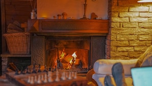 A fireplace with a fire, a chessboard, and a wicker basket. - Charming lux chalet, views, comfort, escape, Samoens Valley, peaceful log fire (Mieussy)