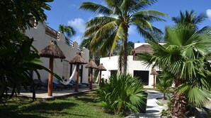A resort with thatched-roof huts, palm trees, and a white building with balconies.