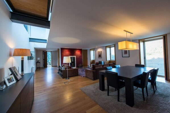 Een ruime woonkamer met een eettafel, comfortabele banken en een groot raam met uitzicht.