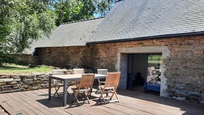 Une terrasse en bois avec une table et des chaises, un mur en pierre et une porte donnant sur un espace extérieur.