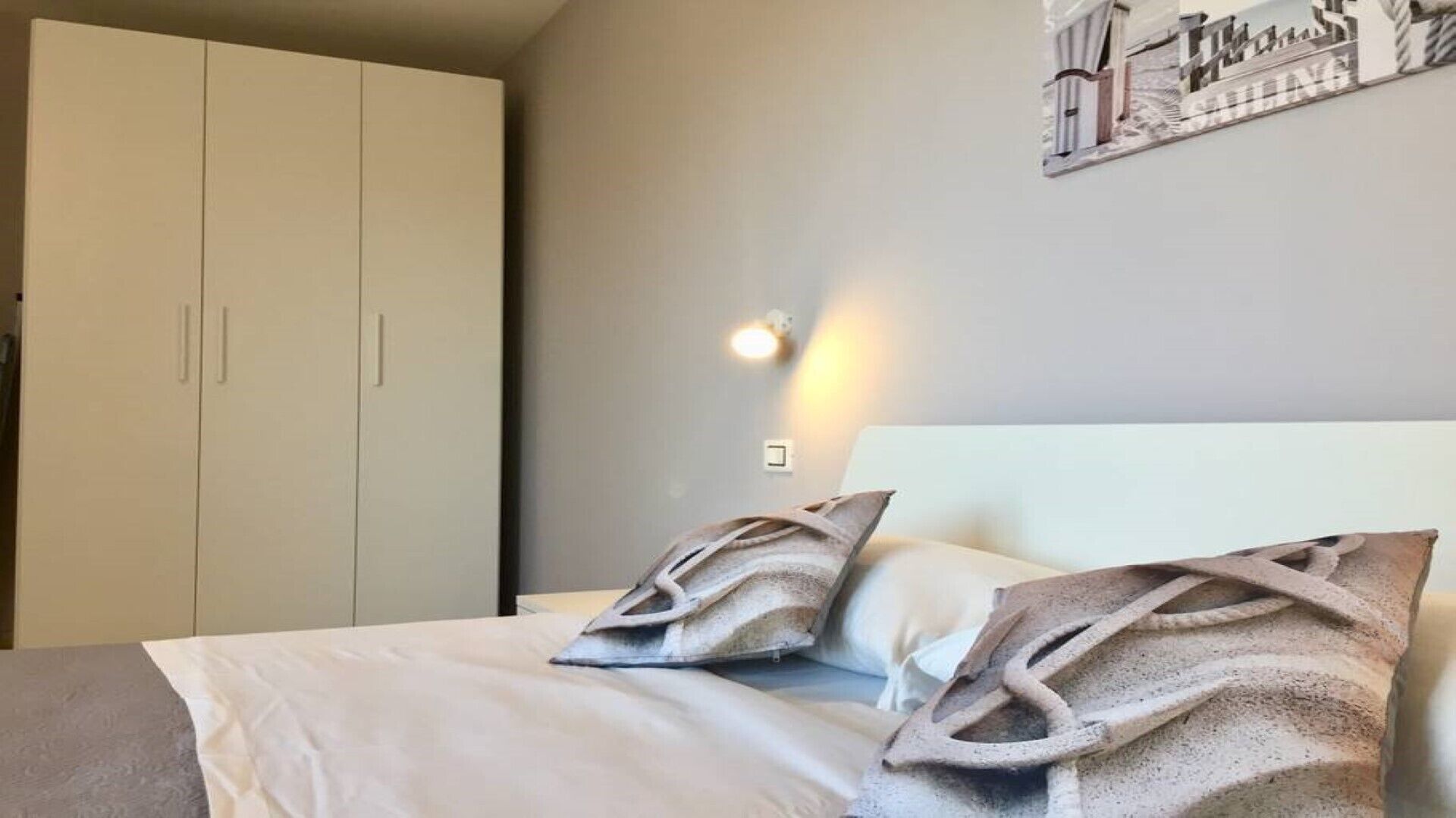 A bedroom with a bed, pillows, a wardrobe, and a wall-mounted light.