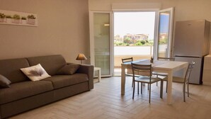 Eine moderne Wohnung mit einem Sofa, einem Esstisch, Stühlen, einer Lampe und einem Kühlschrank.