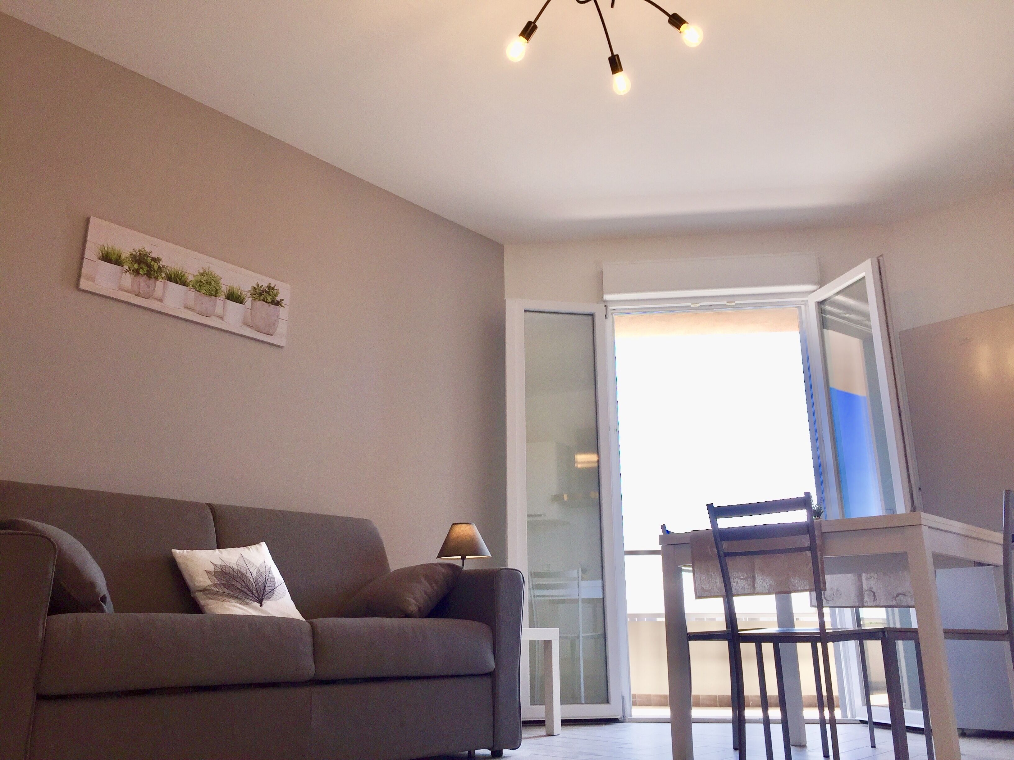 A living room with a sofa, a small table, a lamp, and a chair. There is a sliding glass door leading to an outdoor area.