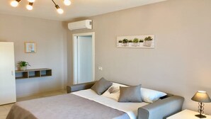 Ein Schlafzimmer mit Bett, Nachttisch, Lampe, Wand-Klimaanlage und einem Regal mit einer Pflanze.