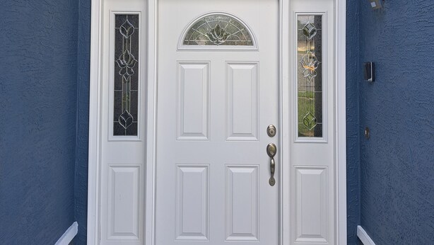 Une porte d’entrée blanche avec un panneau de verre et une fenêtre décorative au-dessus.