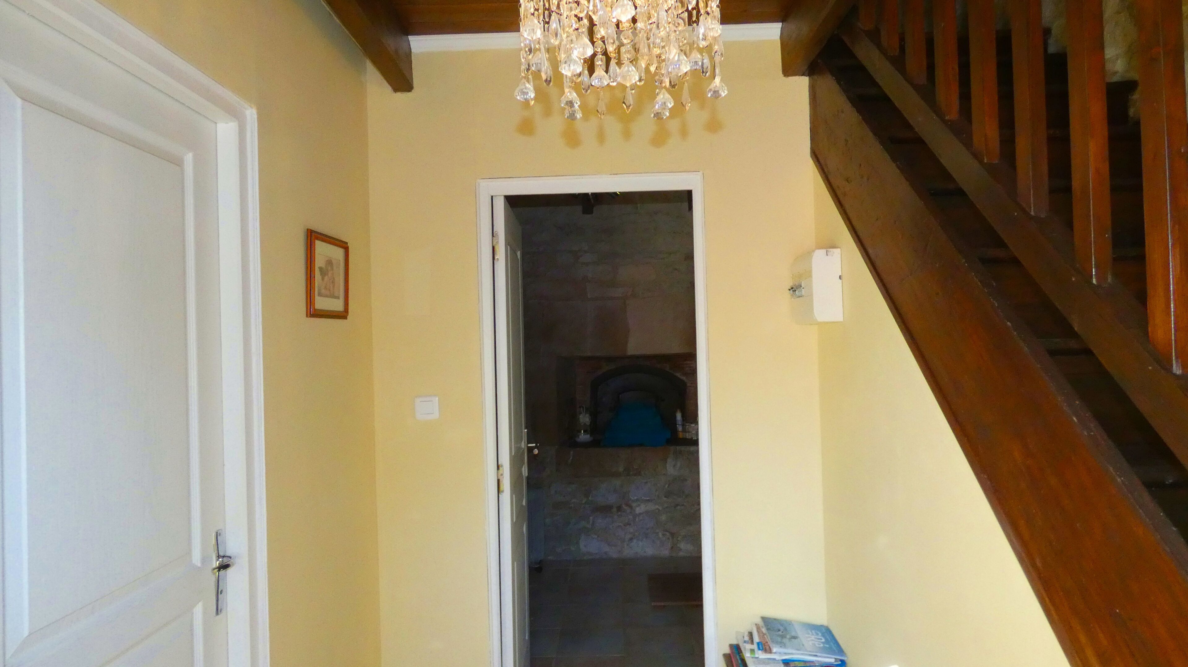 A hallway with a wooden staircase, a door, a framed picture on the wall, and a chandelier.